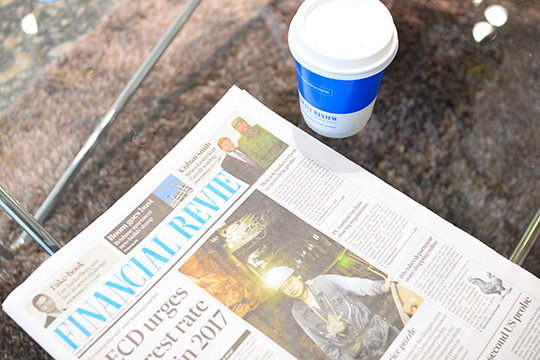 financial review coffee cup advertising next to financial review newspaper