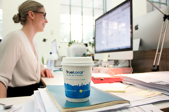 corporate woman at computer taking action to truelocal coffee cup advertising cup